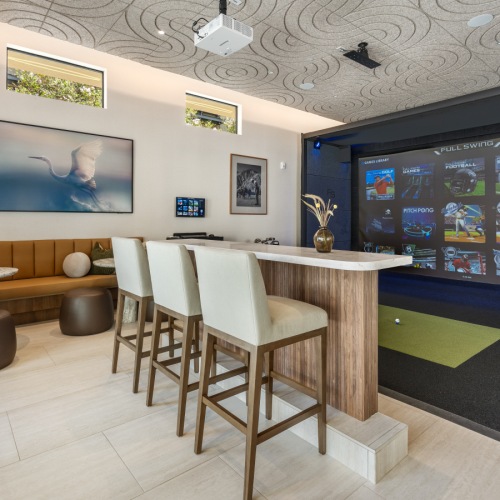Alternate angle of the Lincoln Scottsdale golf lounge bar counter with white barstools and marble top, Full Swing simulator visible at right.